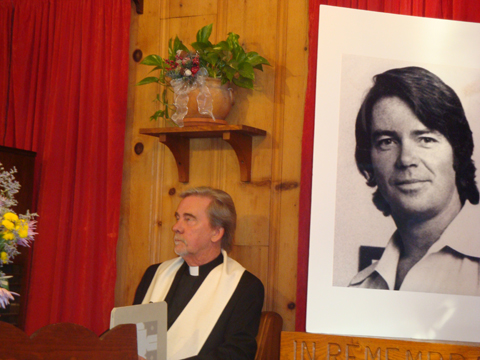 Rev. Charlie Van Dyke beside a big picture of Bill Drake